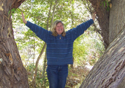 Margareth in a blue sweater standing near a tree